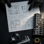 Hands review a building report beside a cracked apartment model and inspection tools.